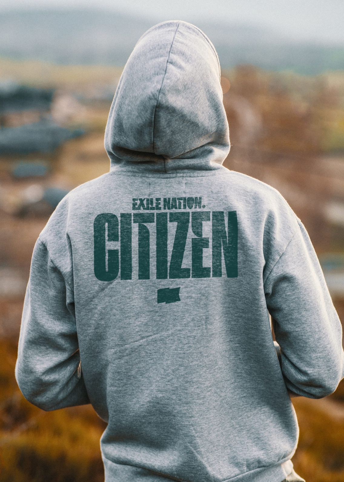 The back of a person wearing a grey Exile Nation Citizen hoodie looking out over nature in the autumn