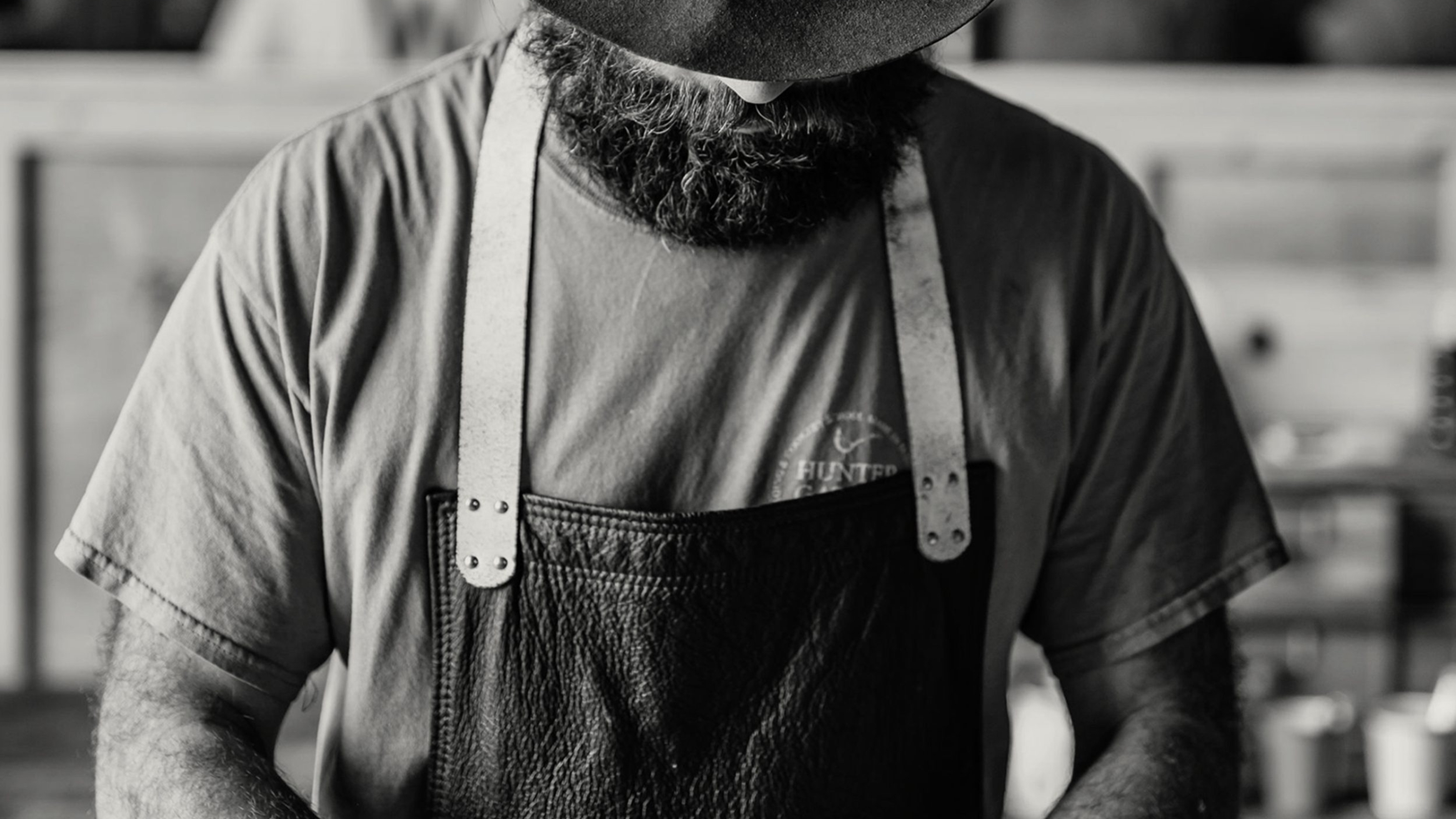Black and white photo of a bearded man cutting up meat