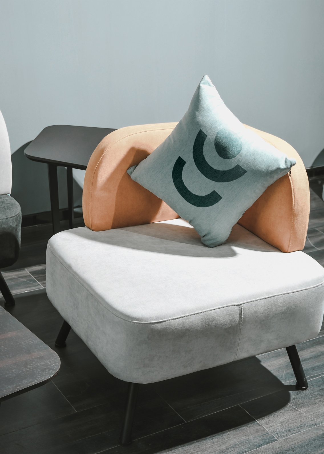 Black abstract brand shapes, printed onto a light grey cushion, which is sat on a modern light grey foot stool. 