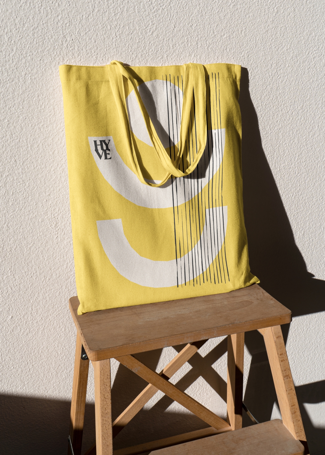 Black and white abstract brand shapes, printed onto a yellow tote bag, which is laying on a wooden stool.