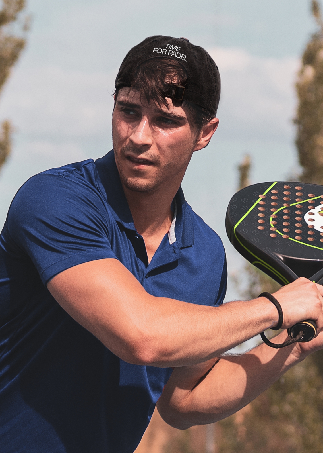 Young man playing padel, with a CorteSport cap on, with 'time for padel' written on the reverse..