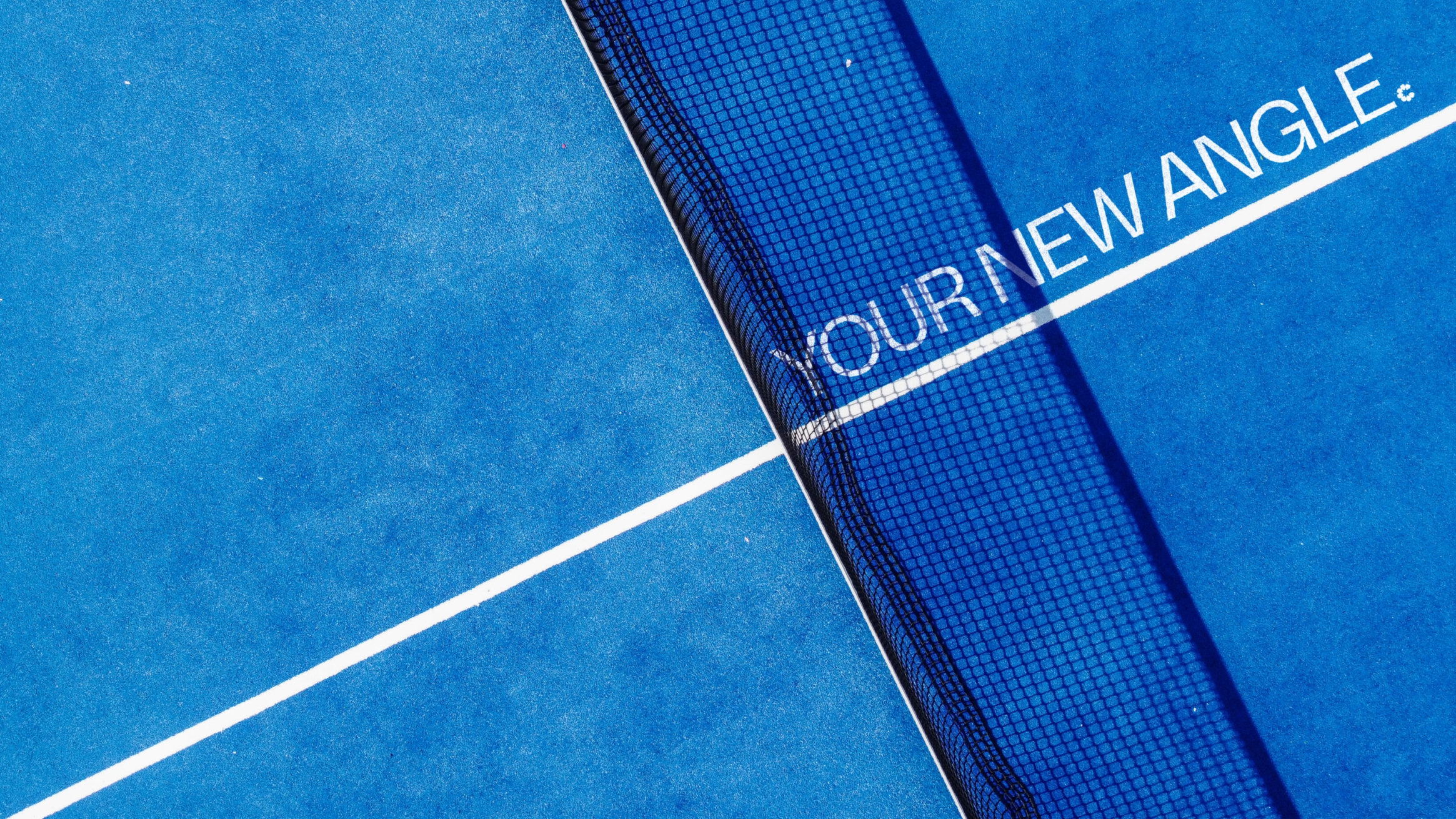 Your New Angle type printed on a blue padel court, running along the white centre line, in the shadow of the net.