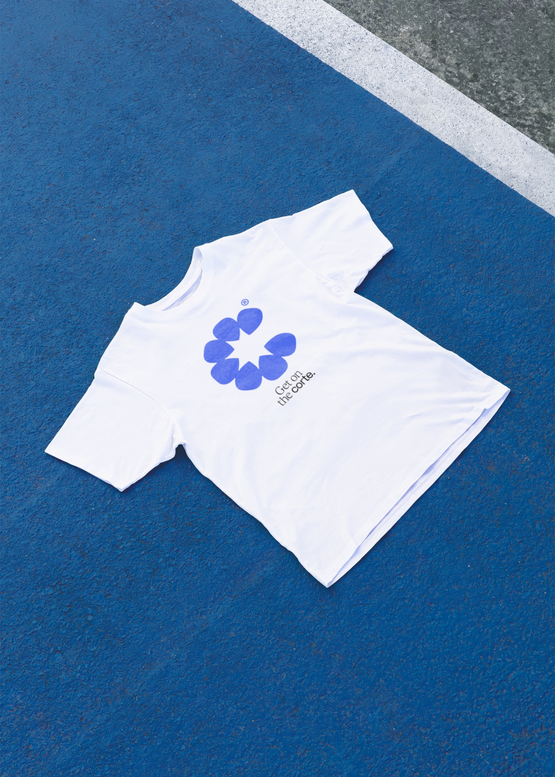 White t-shirt on a blue padel court, with a bright blue icon and 'Get on the Corte' in black text on the front