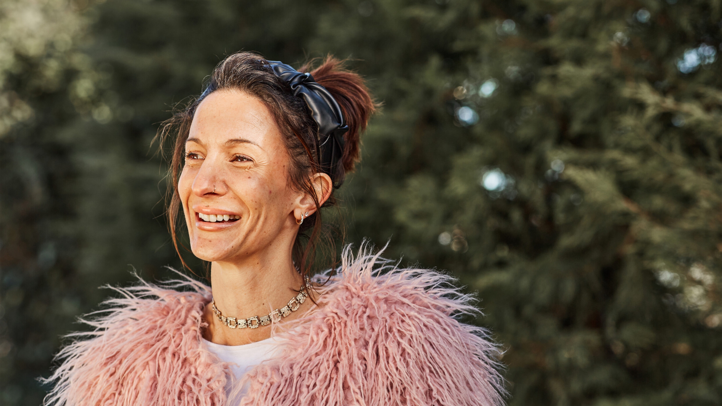 Portrait shot of a young woman smiling, with pink hair and a similar tone roll neck sweater and jacket.