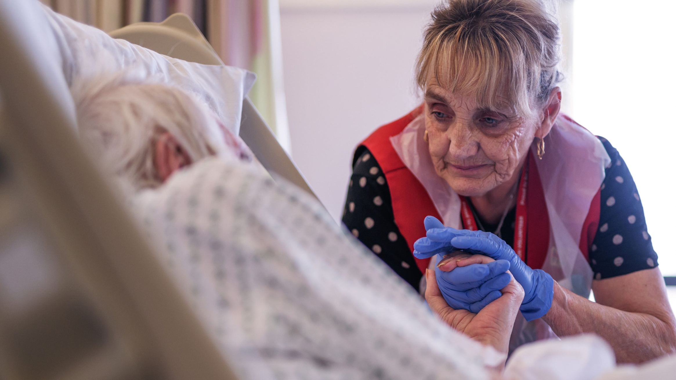 A hospital carer comforting an elderly patient in hospital.