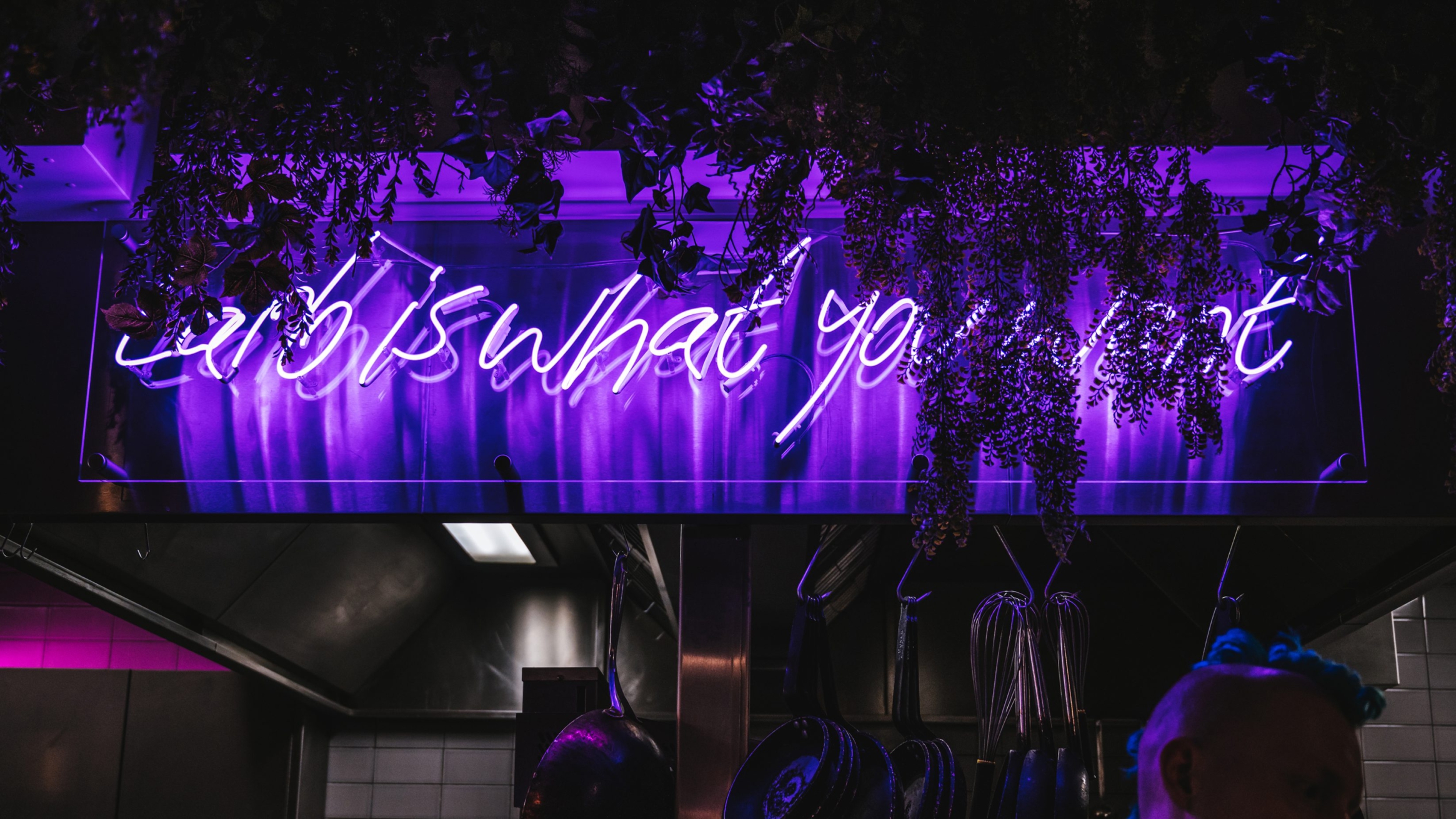 A purple neon sign reading 'larb is what you want' shines through a partial cover of hanging ivy foliage